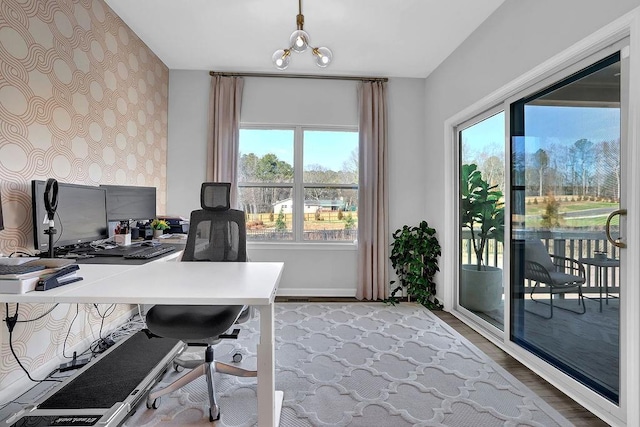 home office with wallpapered walls, baseboards, an accent wall, an inviting chandelier, and light wood-style floors