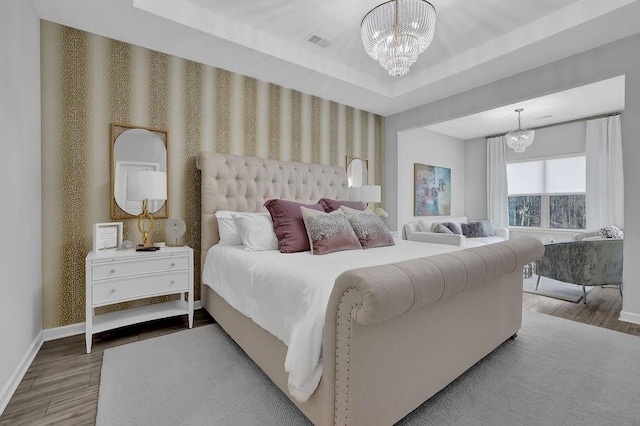 bedroom featuring a notable chandelier, wood finished floors, baseboards, a raised ceiling, and wallpapered walls