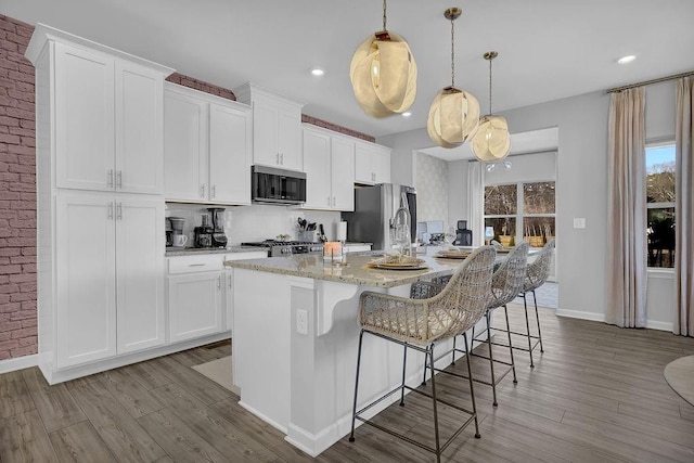 kitchen with stainless steel appliances, an island with sink, wood finished floors, and white cabinets