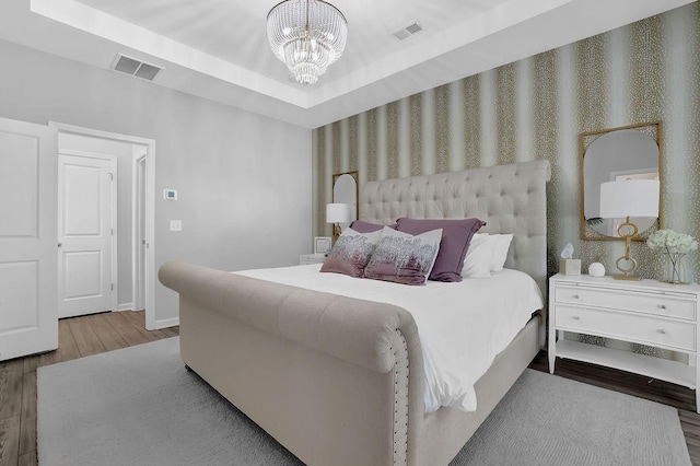 bedroom with a tray ceiling, visible vents, an inviting chandelier, and wood finished floors