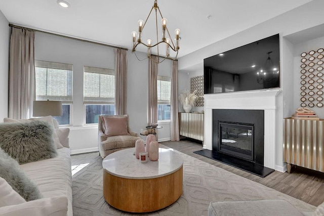 living room featuring wood finished floors, baseboards, radiator, a glass covered fireplace, and an inviting chandelier