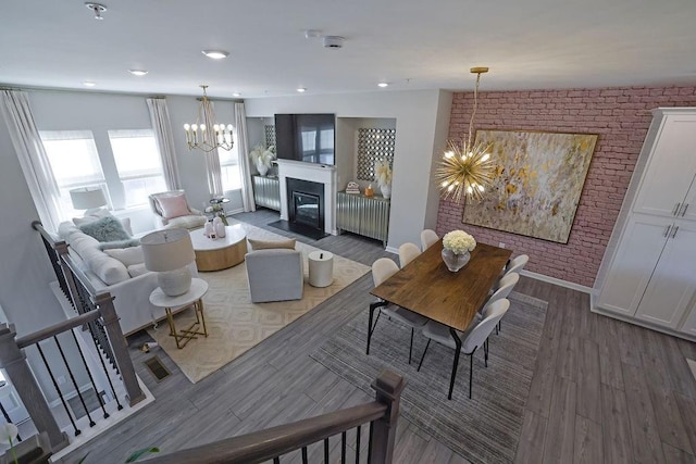 living area with stairs, brick wall, wood finished floors, and an inviting chandelier