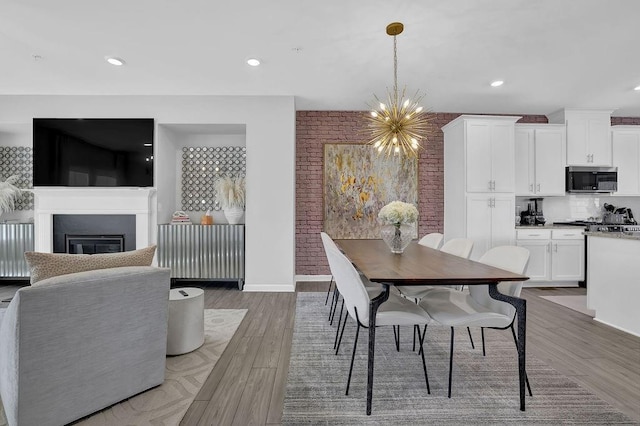 dining space featuring light wood-type flooring, recessed lighting, a chandelier, and a glass covered fireplace