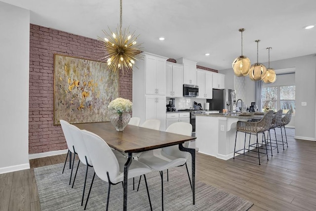 dining room featuring recessed lighting, brick wall, wood finished floors, baseboards, and an inviting chandelier