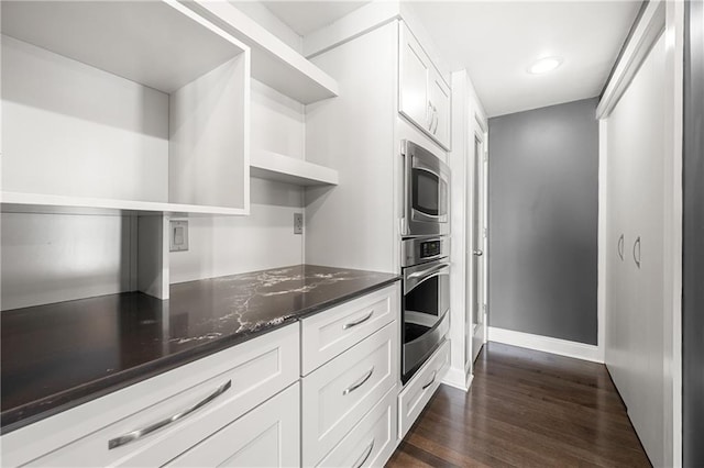 kitchen with white cabinets, dark hardwood / wood-style floors, dark stone countertops, and appliances with stainless steel finishes