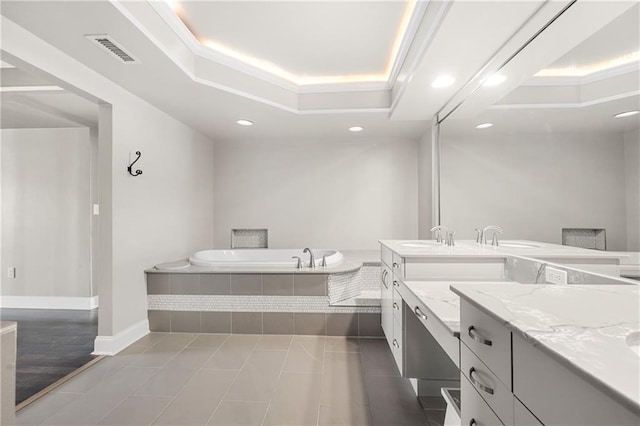 bathroom featuring vanity, tile patterned floors, a raised ceiling, crown molding, and tiled tub