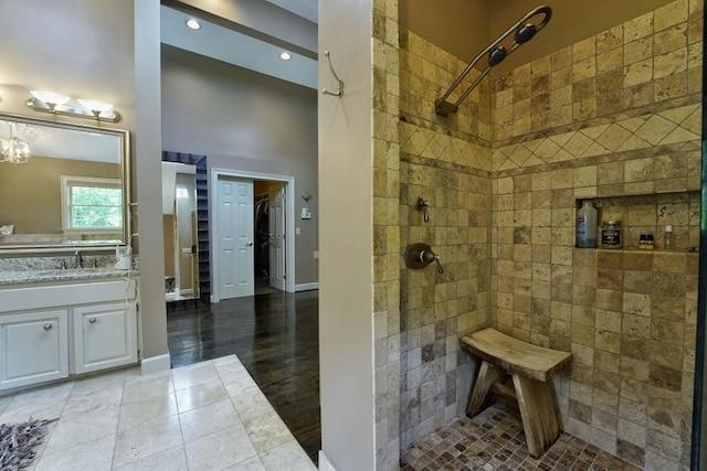 bathroom with tile flooring, a notable chandelier, tiled shower, and vanity with extensive cabinet space