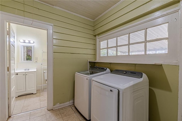 clothes washing area featuring light tile patterned floors, crown molding, sink, washer and dryer, and wood walls