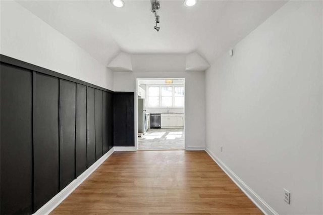 hallway with sink, rail lighting, light hardwood / wood-style floors, and lofted ceiling