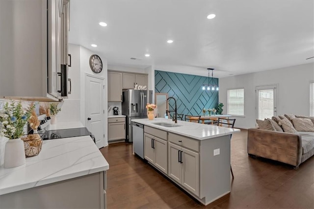 kitchen with sink, appliances with stainless steel finishes, a kitchen island with sink, hanging light fixtures, and dark hardwood / wood-style floors