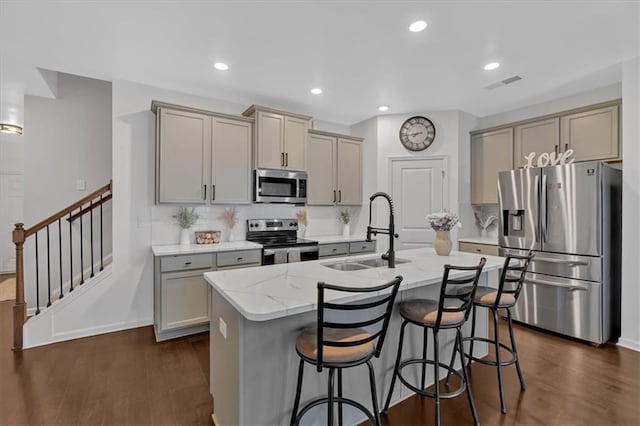 kitchen featuring a kitchen bar, sink, appliances with stainless steel finishes, light stone countertops, and a kitchen island with sink