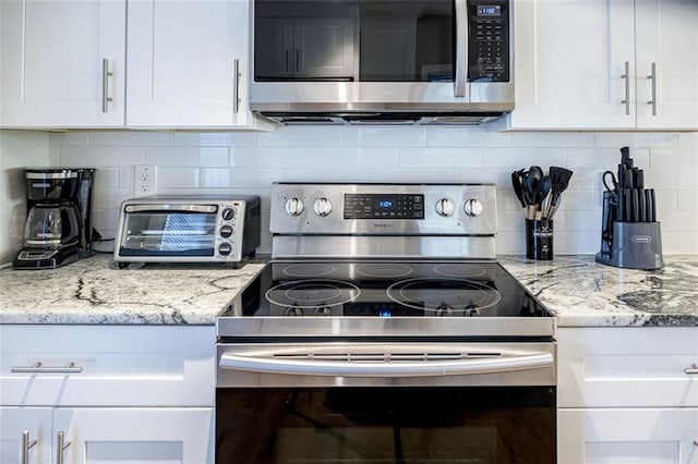 kitchen with appliances with stainless steel finishes, backsplash, white cabinets, and light stone countertops