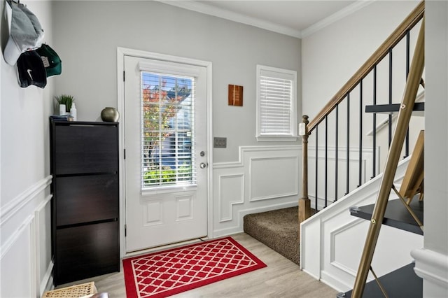 foyer entrance with a wainscoted wall, a decorative wall, stairway, ornamental molding, and wood finished floors