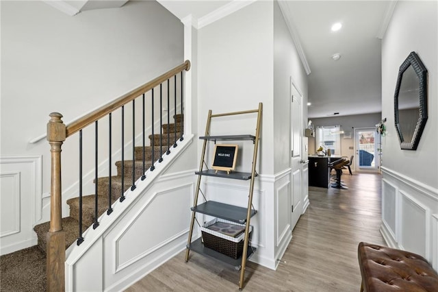 stairs featuring recessed lighting, a decorative wall, wood finished floors, wainscoting, and crown molding