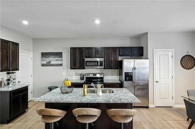 kitchen featuring light stone counters, backsplash, appliances with stainless steel finishes, light wood-style floors, and baseboards