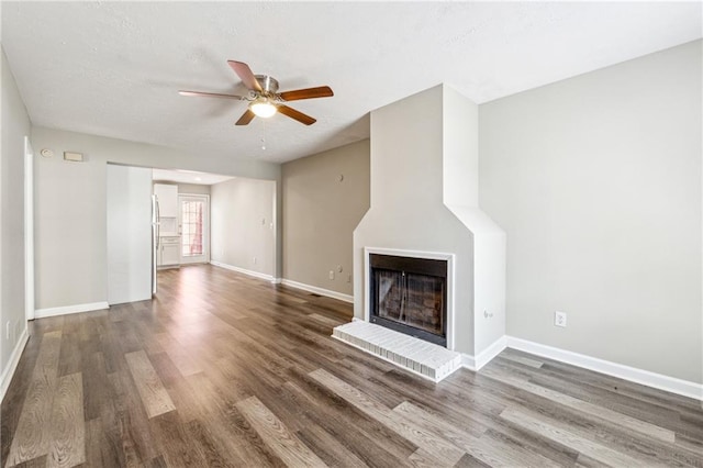 unfurnished living room with wood finished floors, baseboards, ceiling fan, a textured ceiling, and a brick fireplace