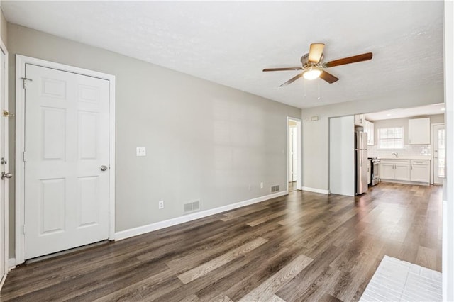 unfurnished living room with visible vents, a ceiling fan, dark wood-style flooring, and baseboards