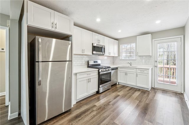 kitchen with white cabinetry, light countertops, wood finished floors, and appliances with stainless steel finishes