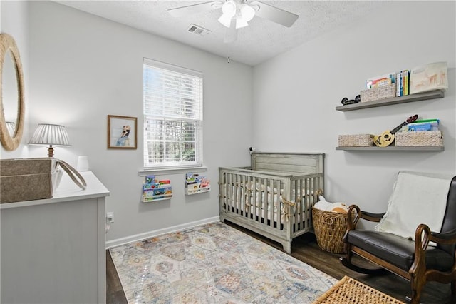 bedroom featuring visible vents, ceiling fan, wood finished floors, a textured ceiling, and a nursery area