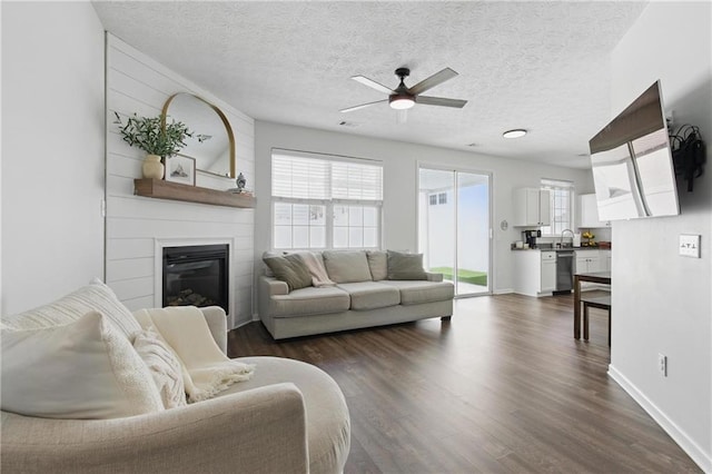 living room with a fireplace, a textured ceiling, ceiling fan, and dark wood-style flooring