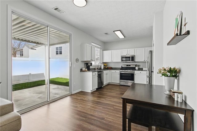 kitchen featuring a sink, dark countertops, stainless steel appliances, white cabinets, and dark wood-style flooring