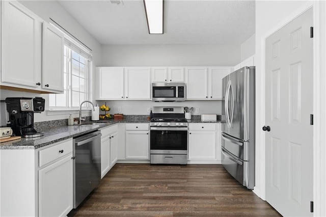 kitchen with a sink, dark wood finished floors, white cabinetry, stainless steel appliances, and dark stone counters