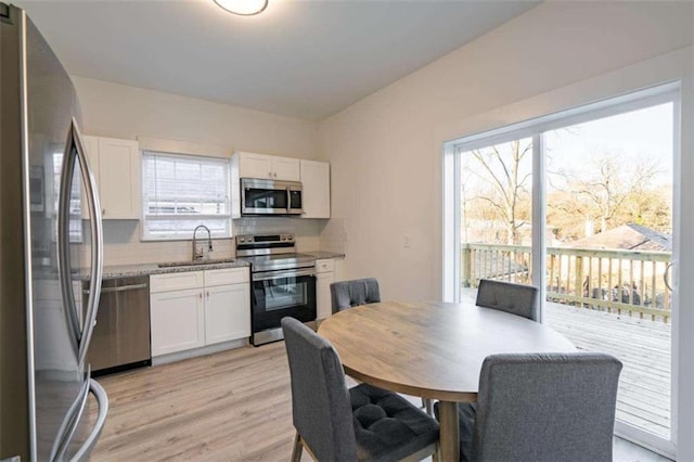 kitchen with light wood-type flooring, decorative backsplash, stainless steel appliances, white cabinetry, and a sink