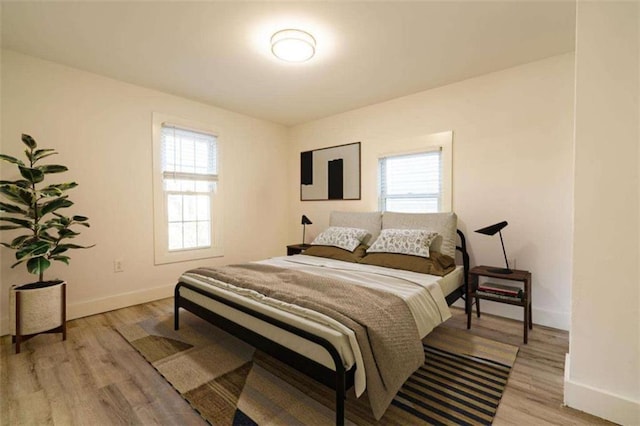 bedroom with multiple windows, light wood-type flooring, and baseboards