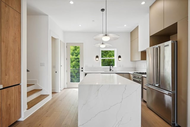 kitchen featuring sink, hanging light fixtures, a center island, high end appliances, and light stone counters