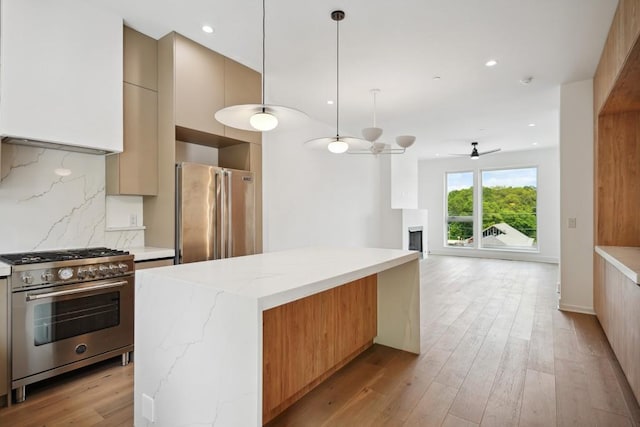 kitchen featuring light stone counters, tasteful backsplash, hanging light fixtures, premium appliances, and light hardwood / wood-style floors