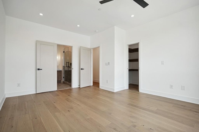 unfurnished bedroom featuring ensuite bathroom, a spacious closet, ceiling fan, light wood-type flooring, and a closet