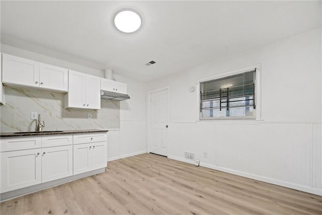 kitchen with decorative backsplash, white cabinetry, sink, and light hardwood / wood-style flooring