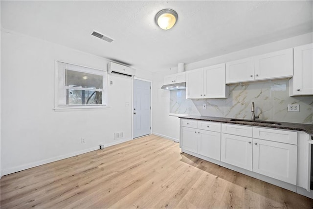 kitchen with decorative backsplash, white cabinetry, sink, and a wall mounted AC