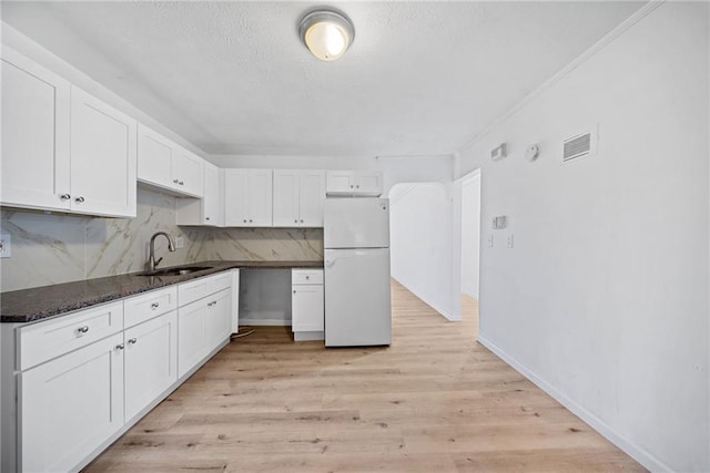 kitchen with white fridge, white cabinetry, dark stone countertops, and sink