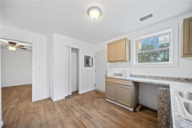 kitchen featuring light stone countertops, light brown cabinetry, ceiling fan, wood-type flooring, and built in desk