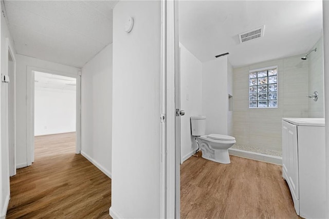 bathroom featuring hardwood / wood-style floors, toilet, and a tile shower