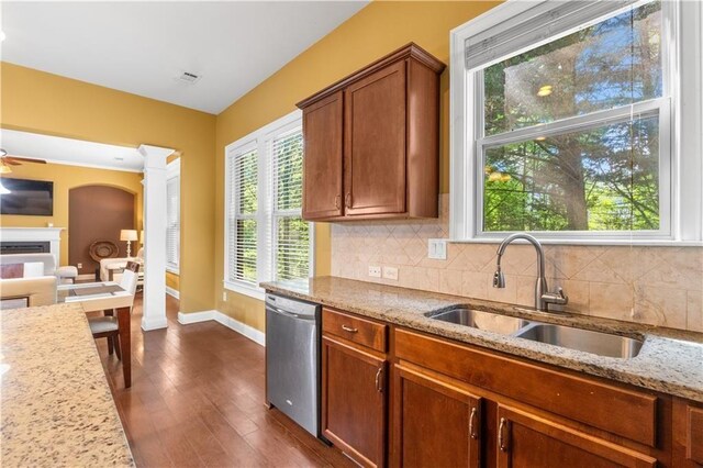 kitchen featuring baseboards, a sink, a fireplace, light stone countertops, and stainless steel dishwasher