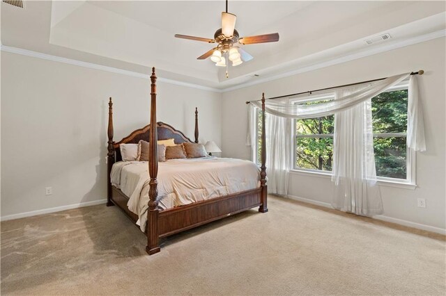 bedroom with light carpet, a tray ceiling, baseboards, and crown molding