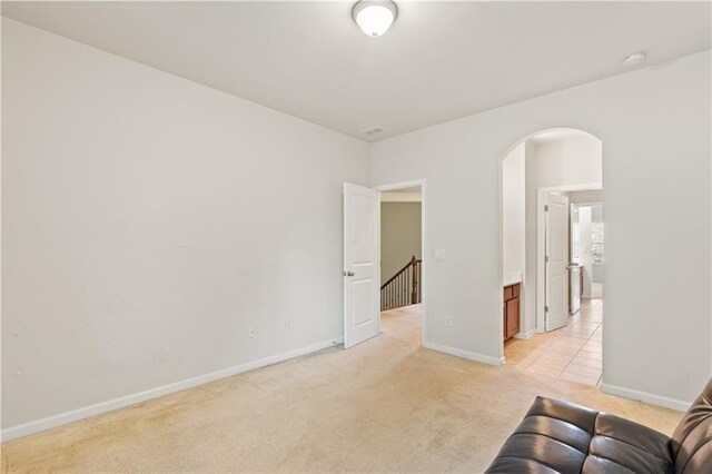unfurnished living room featuring baseboards, arched walkways, and light colored carpet
