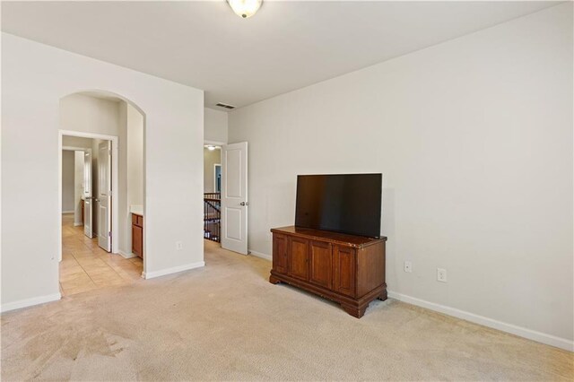 unfurnished living room featuring arched walkways, light colored carpet, and baseboards