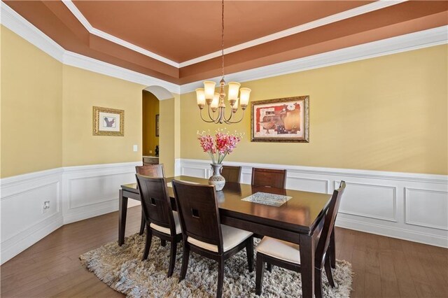 dining space featuring a chandelier, arched walkways, wood-type flooring, and a tray ceiling