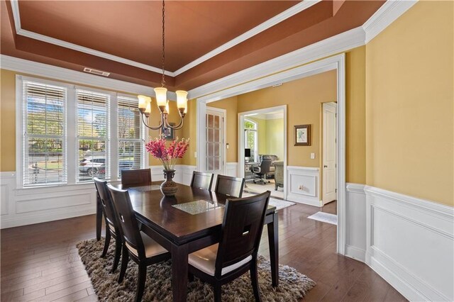 dining space with crown molding, a tray ceiling, a notable chandelier, and wainscoting