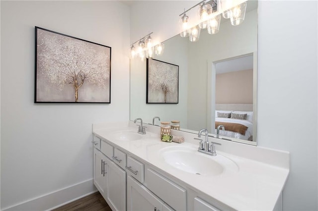 ensuite bathroom featuring double vanity, baseboards, a sink, and wood finished floors
