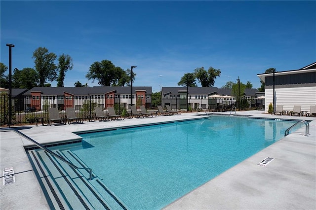 community pool with a patio, fence, and a residential view