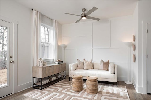 sitting room with a ceiling fan, a decorative wall, and wood finished floors