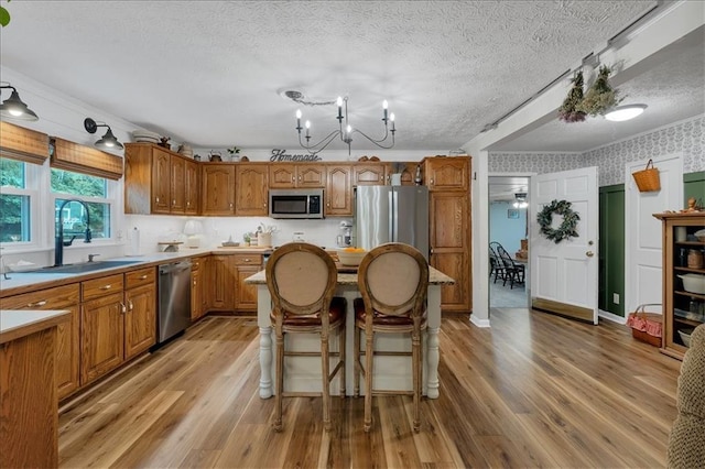 kitchen with pendant lighting, a textured ceiling, stainless steel appliances, sink, and light hardwood / wood-style flooring