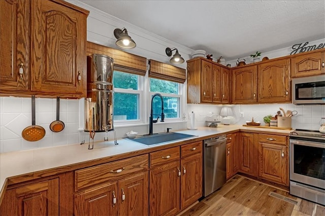 kitchen with decorative backsplash, sink, crown molding, light hardwood / wood-style flooring, and appliances with stainless steel finishes