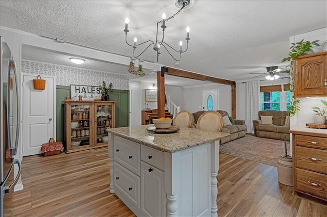 kitchen with a textured ceiling, white cabinets, a kitchen island, stainless steel refrigerator, and light hardwood / wood-style flooring