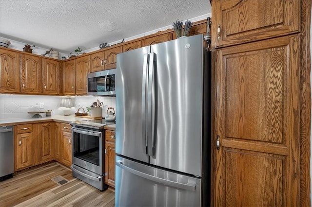 kitchen with light wood-type flooring, backsplash, stainless steel appliances, and a textured ceiling