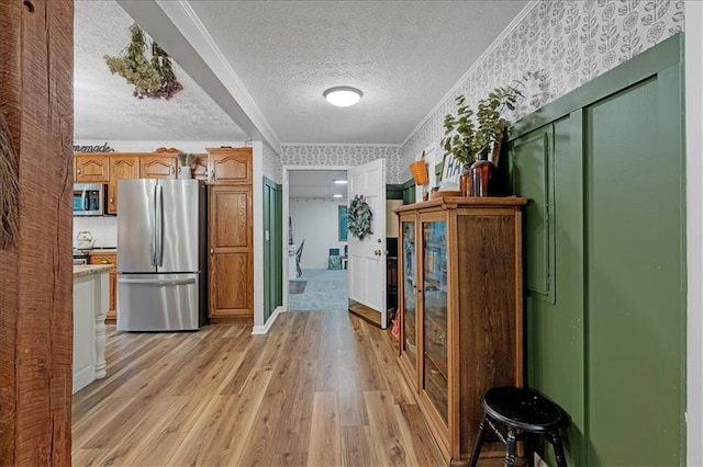 hallway featuring light wood-type flooring, ornamental molding, and a textured ceiling